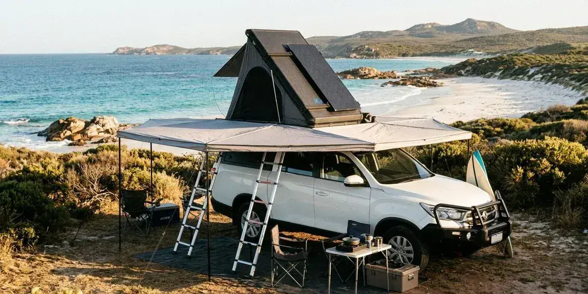 A dual-cab 4WD camper with rooftop tent and 270 degree awning parked at a scenic coastal campsite in Western Australia with solar panels visible on the roof