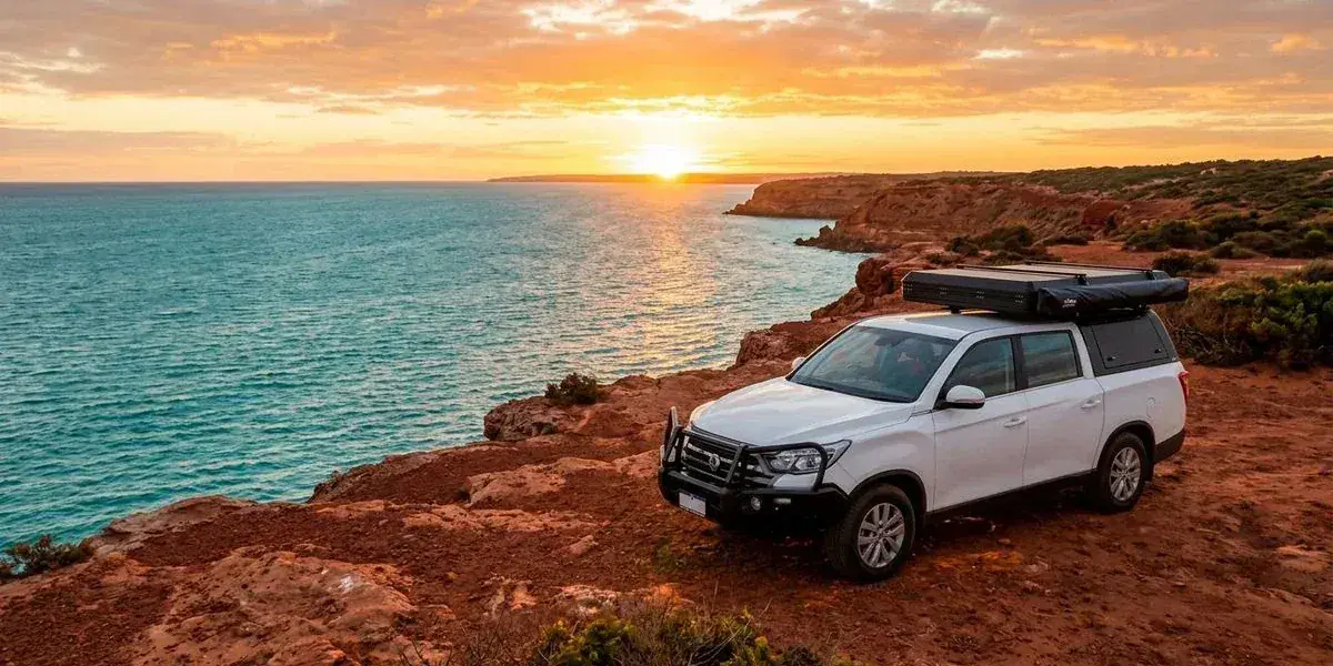 Rooftop tent camper parked on red coastal cliffs overlooking the turquoise Indian Ocean at sunset along the Western Australian Coral Coast